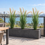 Three artificial reed grass plants in a long outdoor trough planter