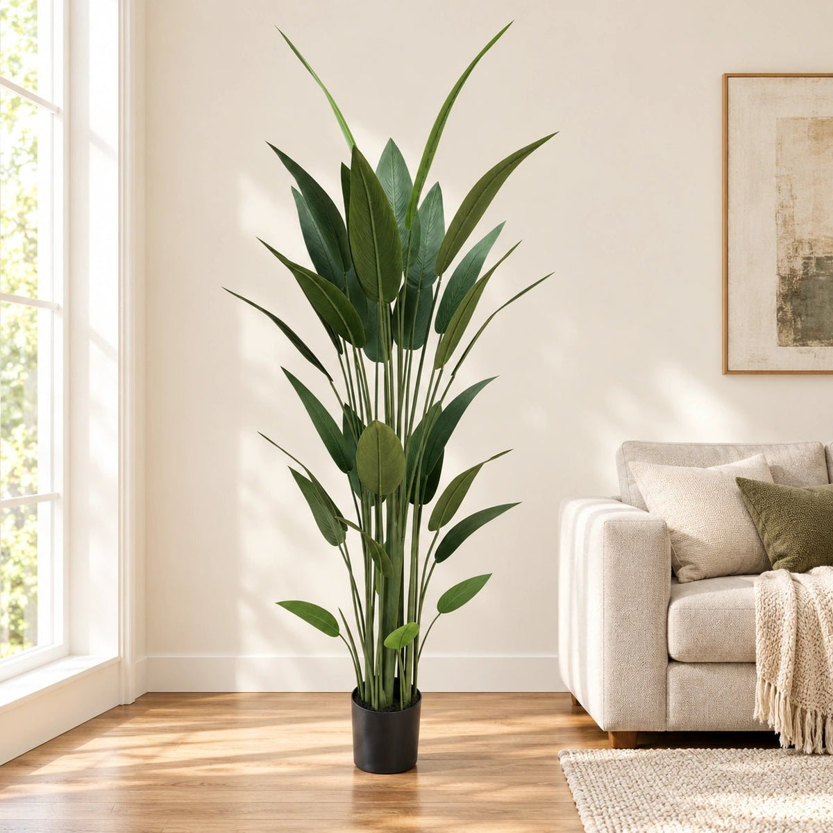 A tall artificial green plant with long, slender leaves in a black pot, styled in a bright living room next to a beige sofa.