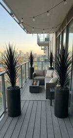Outdoor patio with furniture, plants, and a fire pit on a balcony with cityscape view.