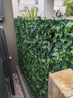 Artificial green wall panel with ivy-like leaves on a building exterior.