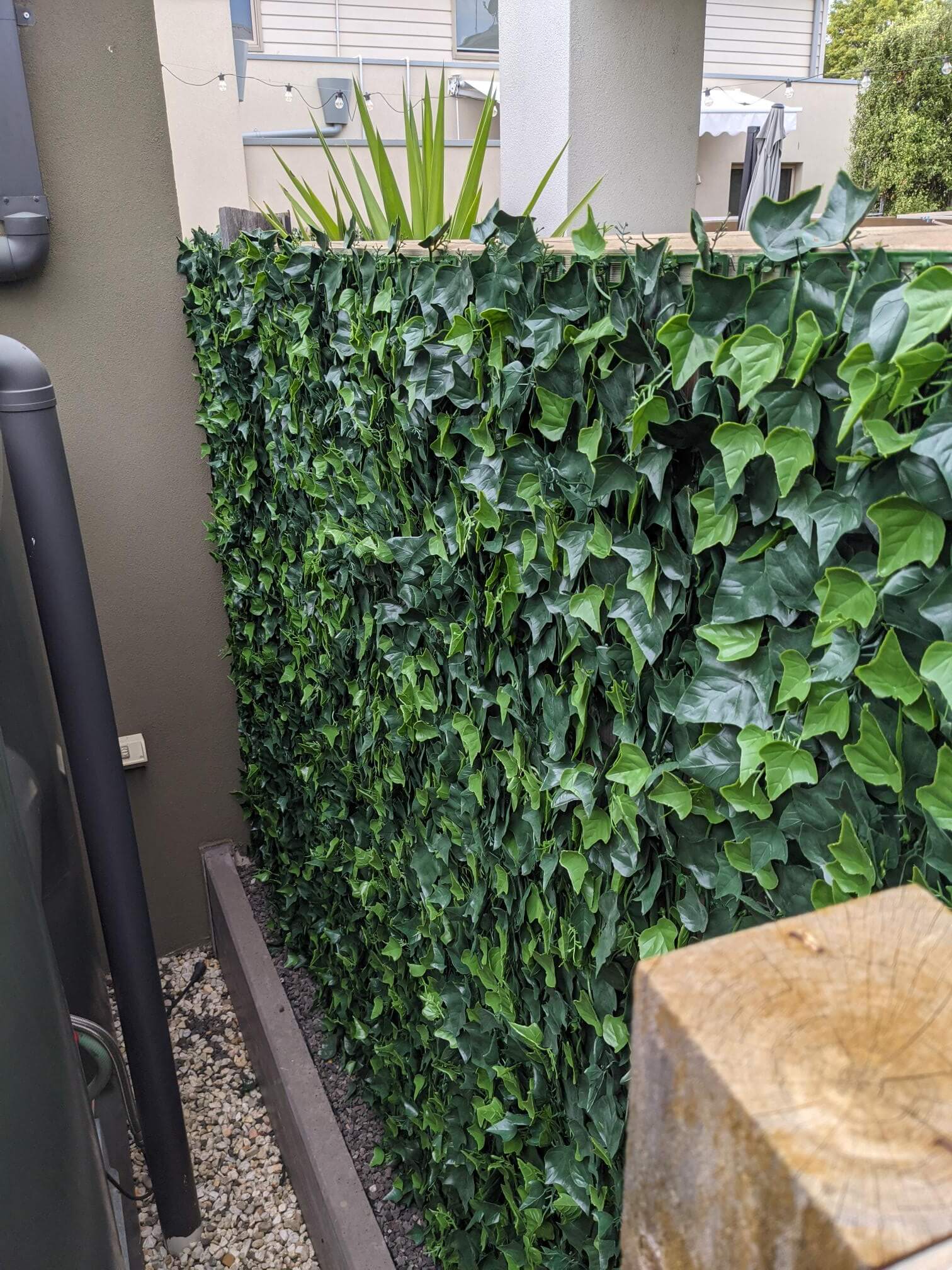Artificial green wall panel with ivy-like leaves on a building exterior.