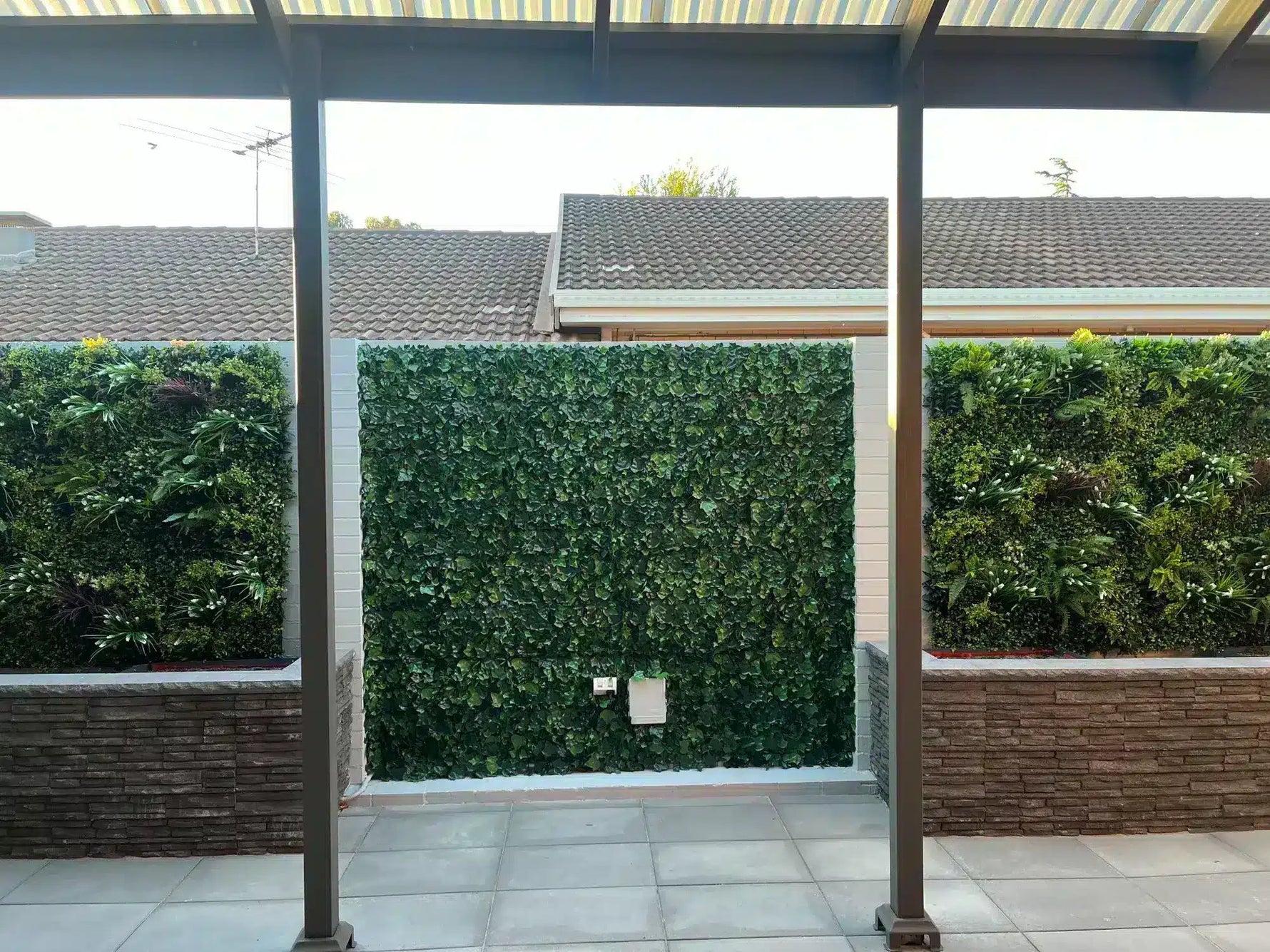 Patio area with glass panels, green hedges, and tiled floor.