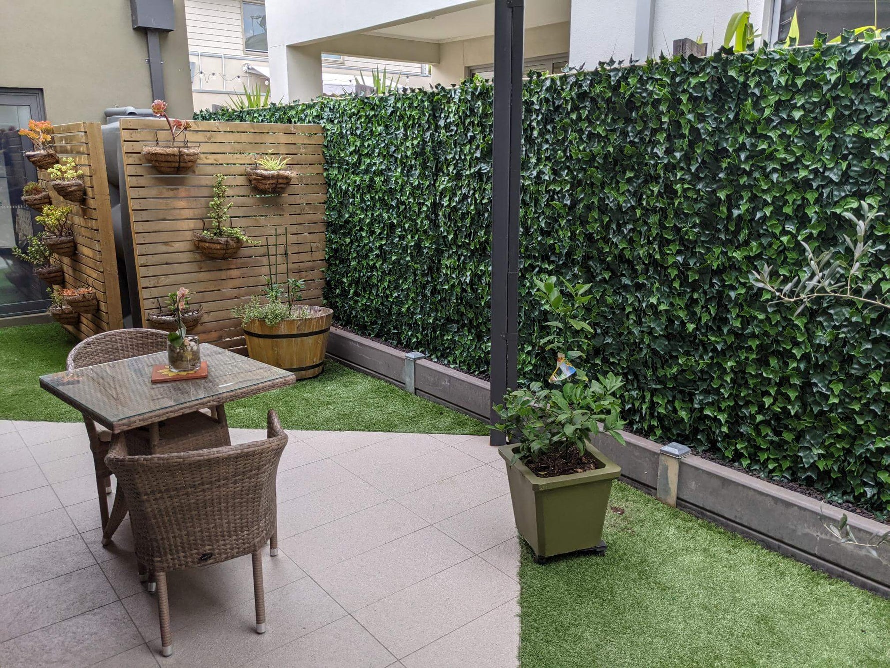 Outdoor patio area with a table, chairs, and potted plants against a green hedge.
