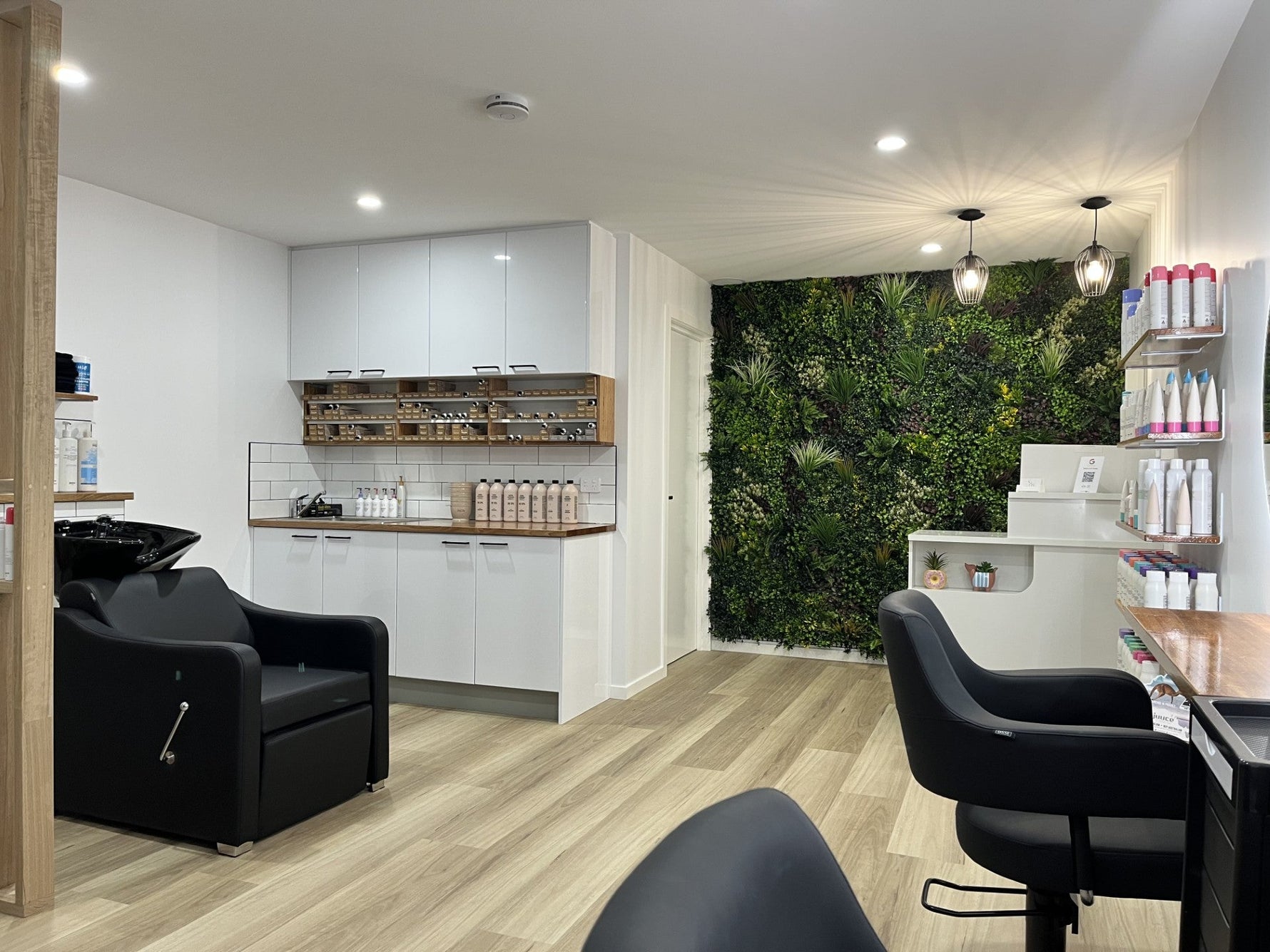 Modern salon interior with black chairs, white cabinets, and a green wall feature.