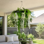 Hanging greenery and white flowers in a decorative pot on a patio with outdoor furniture.
