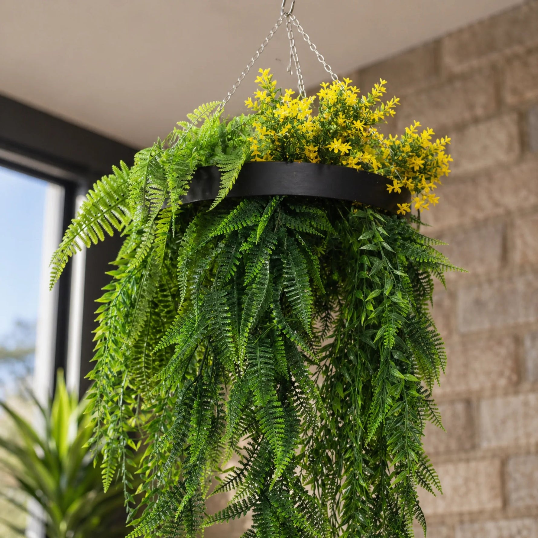 Hanging basket with green ferns and yellow flowers against a brick wall.