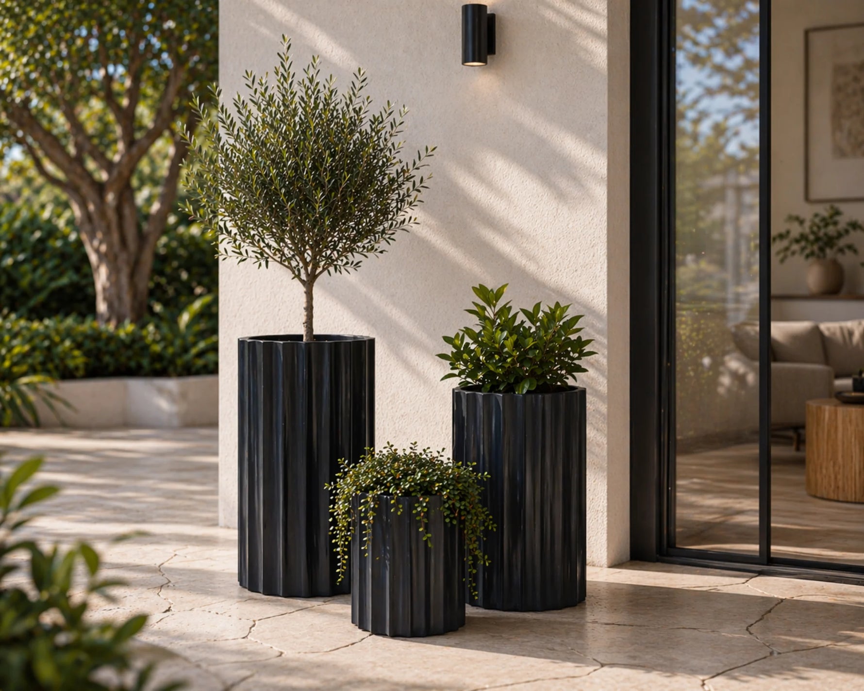 Three black cylindrical planters with green plants on a patio area.