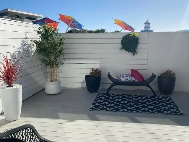 Outdoor patio area with a bench, potted plants, and colorful umbrellas on a clear day.