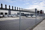 Commercial building with cars parked outside, viewed through a chain-link fence.