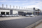 Commercial building with cars parked in front, viewed through a chain-link fence.