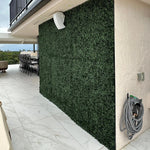 Outdoor patio area with artificial green wall and garden hose on a white wall.