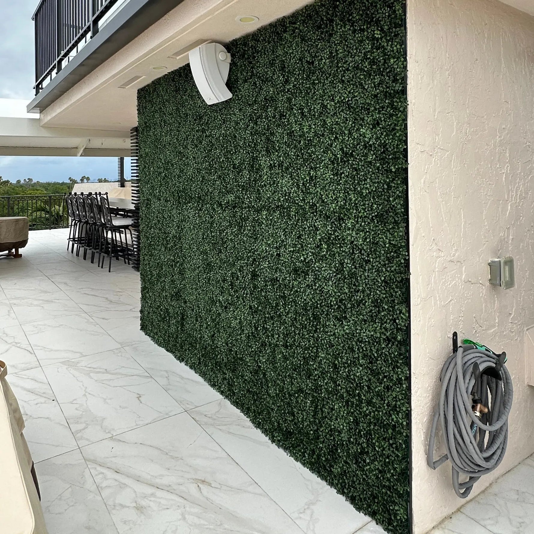 Outdoor patio area with artificial green wall and garden hose on a white wall.