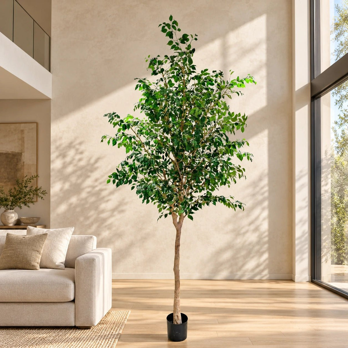 A tall artificial potted tree with green leaves and a light brown trunk, standing in a black pot on a wooden floor in a modern living room setting.