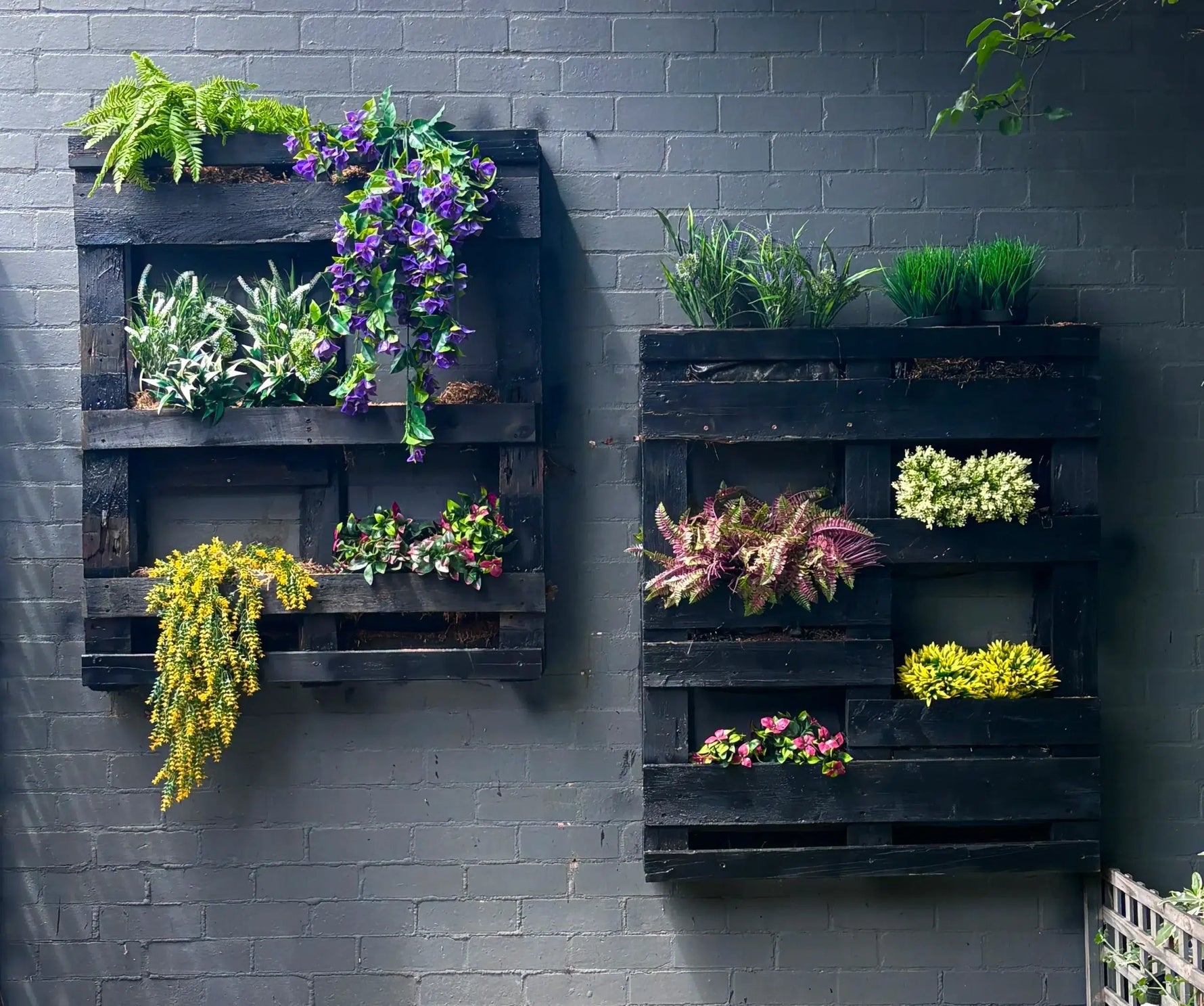 Wall-mounted wooden planters with various plants against a gray brick wall.