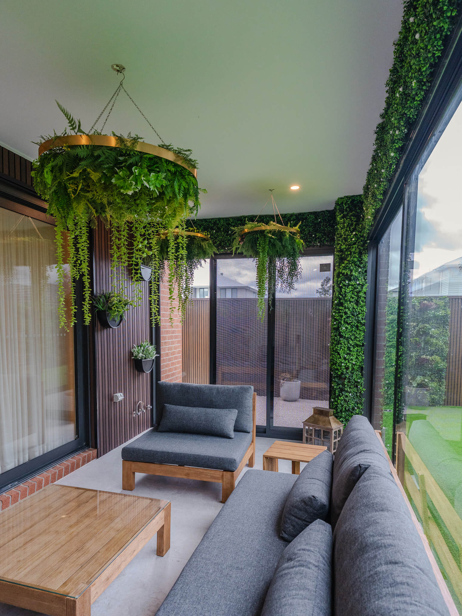 Modern outdoor living space with gray sofa, wooden coffee table, and hanging plants.