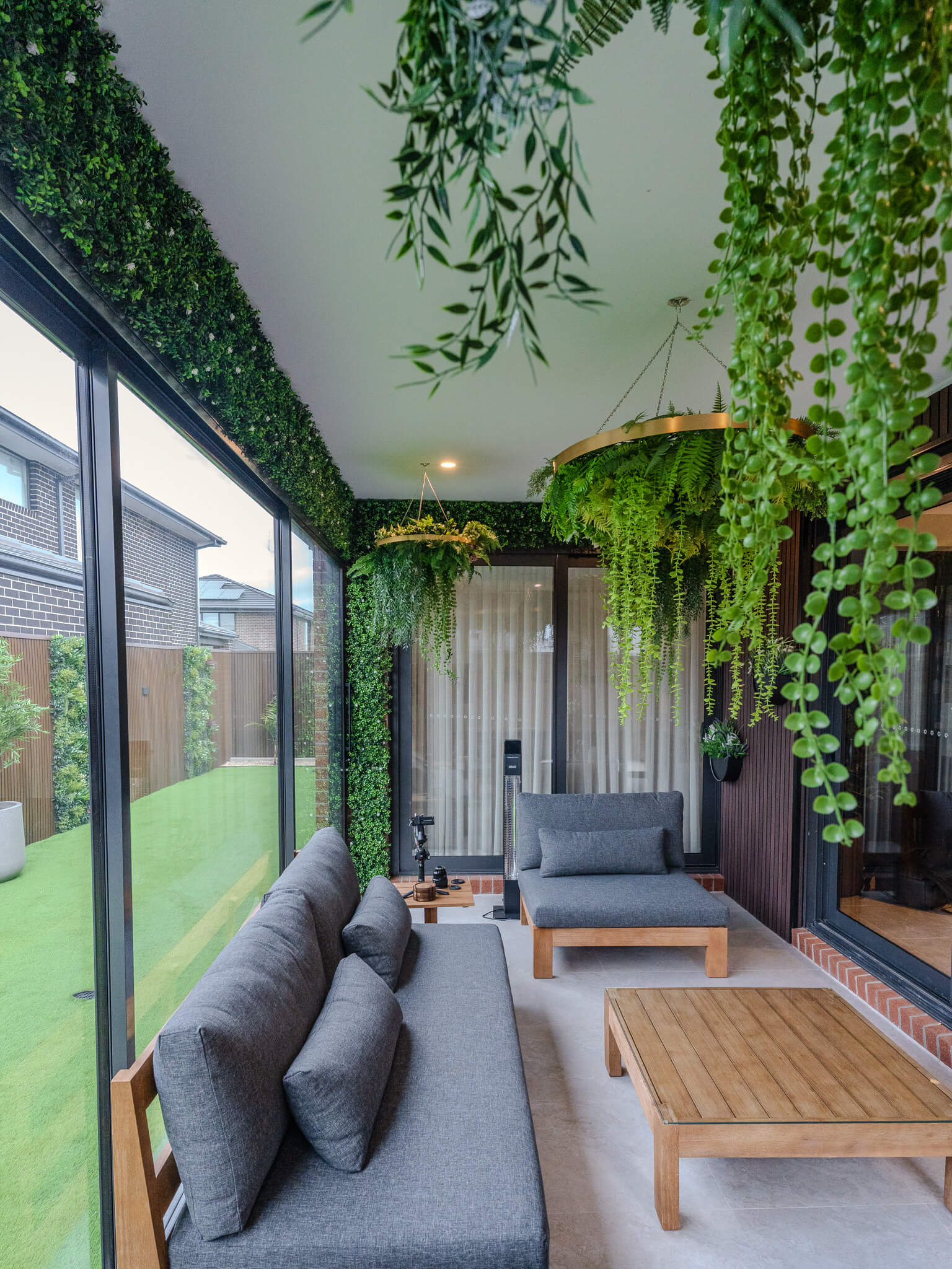 Modern outdoor living space with gray sofa, wooden coffee table, and greenery.