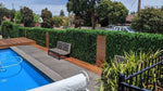 Pool area with wooden deck, bench, and greenery