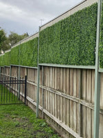 Wooden fence with green artificial hedge panels on a cloudy day