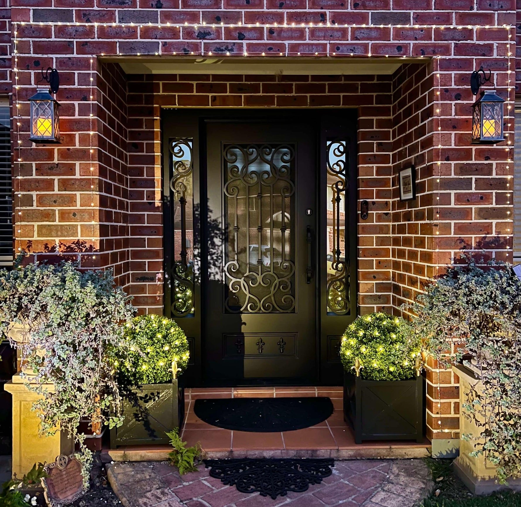 Decorative front door with ornate design on a brick wall, illuminated by outdoor lights.
