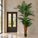 A tall artificial palm tree in a black pot, positioned in a grand stone lobby next to dark double doors.