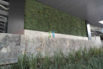 Green artificial grass wall on a stone ledge with a building in the background