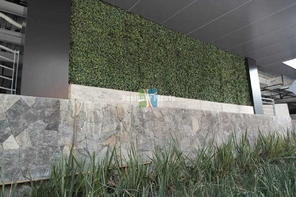 Green artificial grass wall on a stone ledge with a building in the background