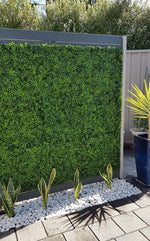 Artificial green wall panel in a garden setting with plants and pebbles.