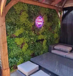 Neon sign reading 'Good Times' on a green living wall with outdoor furniture.