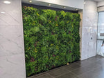 Green living wall in an indoor setting with marble walls and a glass door.