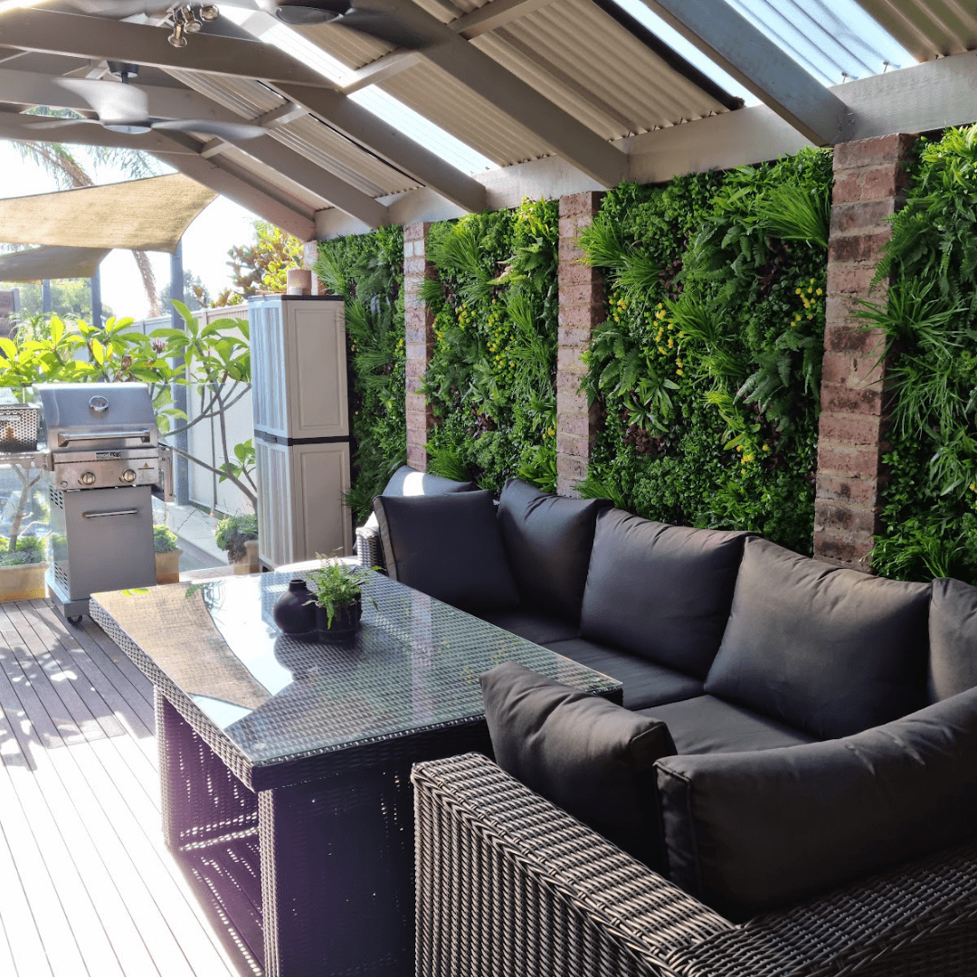 Outdoor patio with black sectional sofa, glass table, and greenery wall.