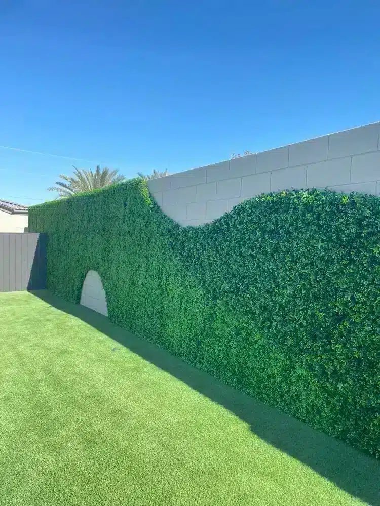 Artificial green hedge against a gray wall with clear blue sky