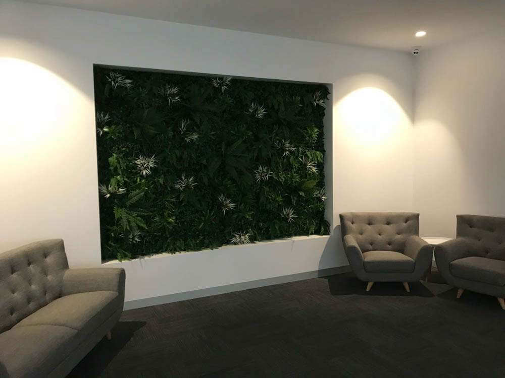 Modern interior with gray sofa and chairs against a wall with green foliage.