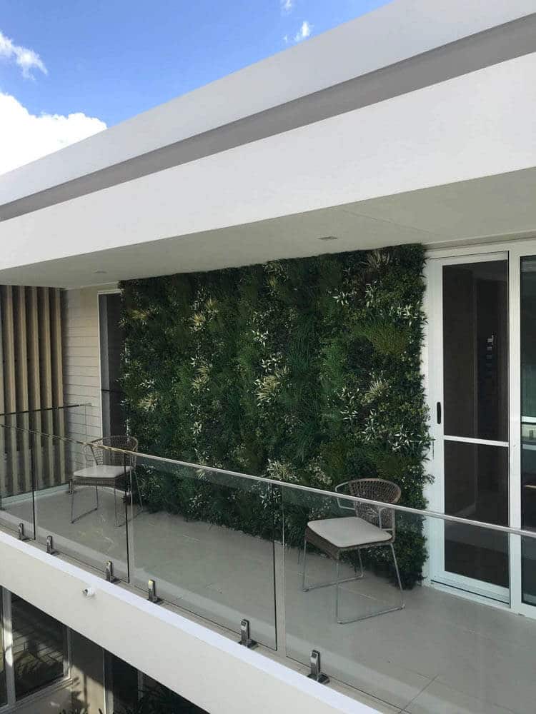 Balcony with glass railing and green wall, featuring a chair and table.