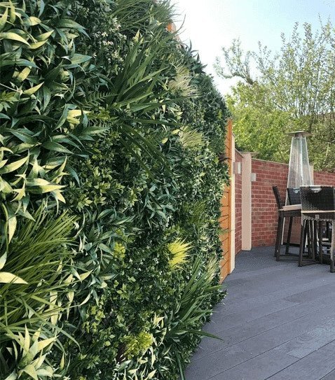 Tall green hedge with a patio area and outdoor furniture in the background