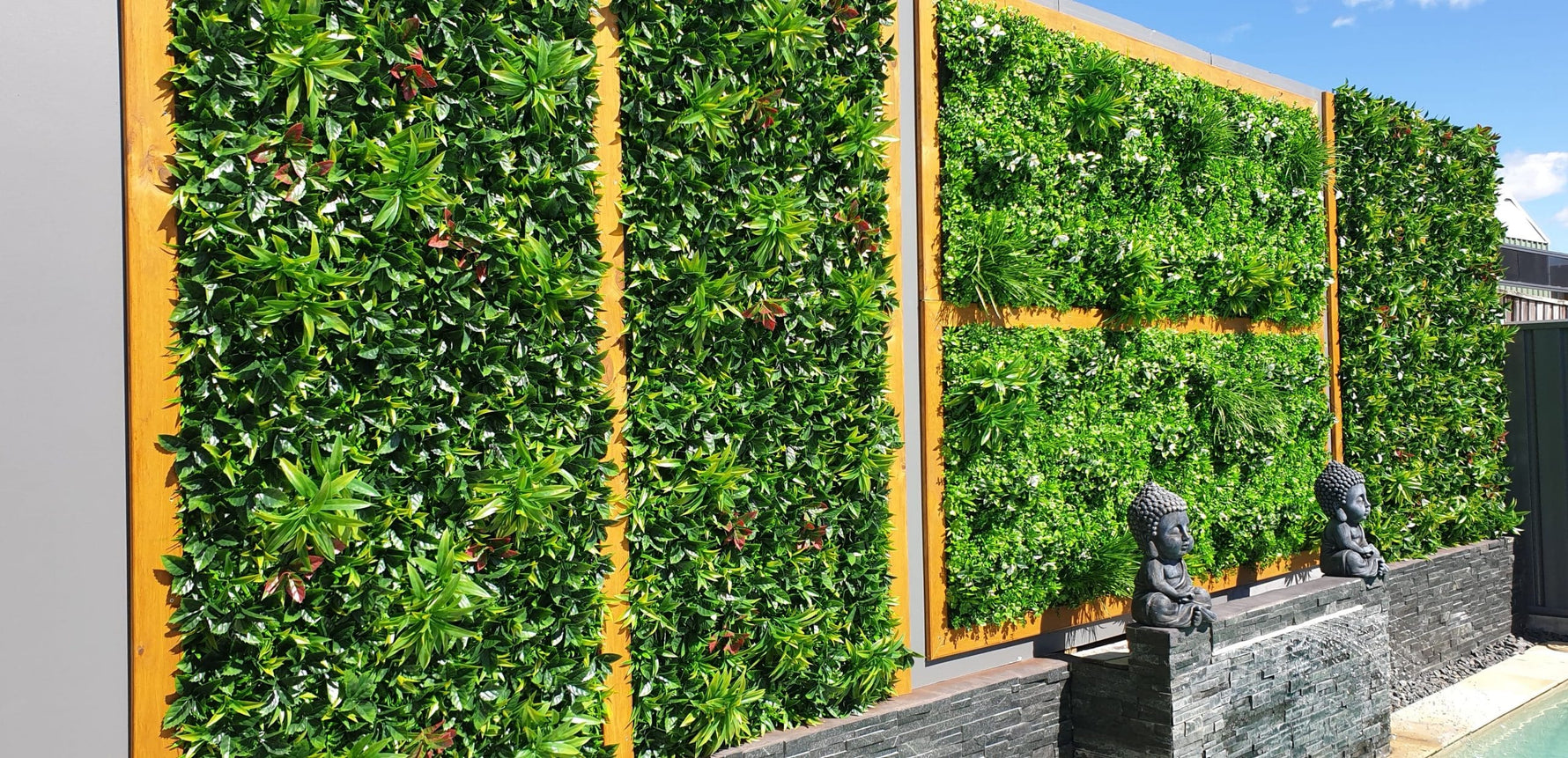 Green artificial wall with gold frame and stone statues on a building exterior.