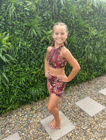 Young girl in a leopard print swimsuit standing in front of green foliage.