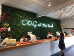 Neon sign 'COG at the trunk' above a counter with people in a modern interior setting.