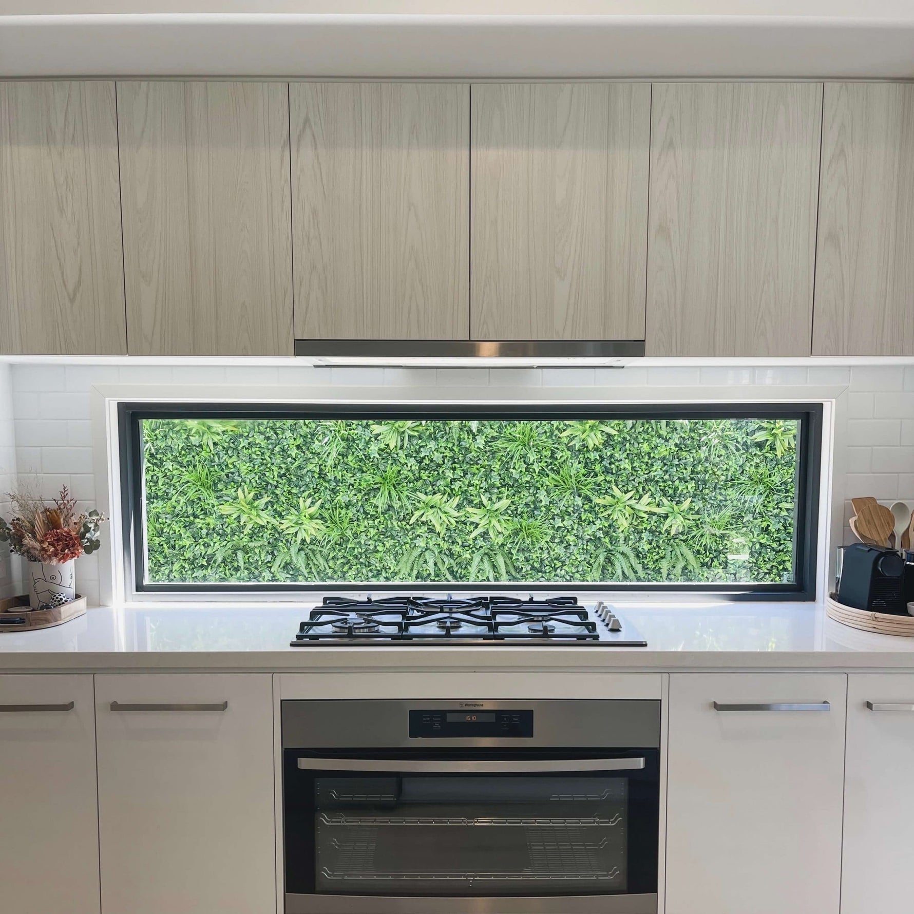 Modern kitchen with light wood cabinets, gas stove, and oven.
