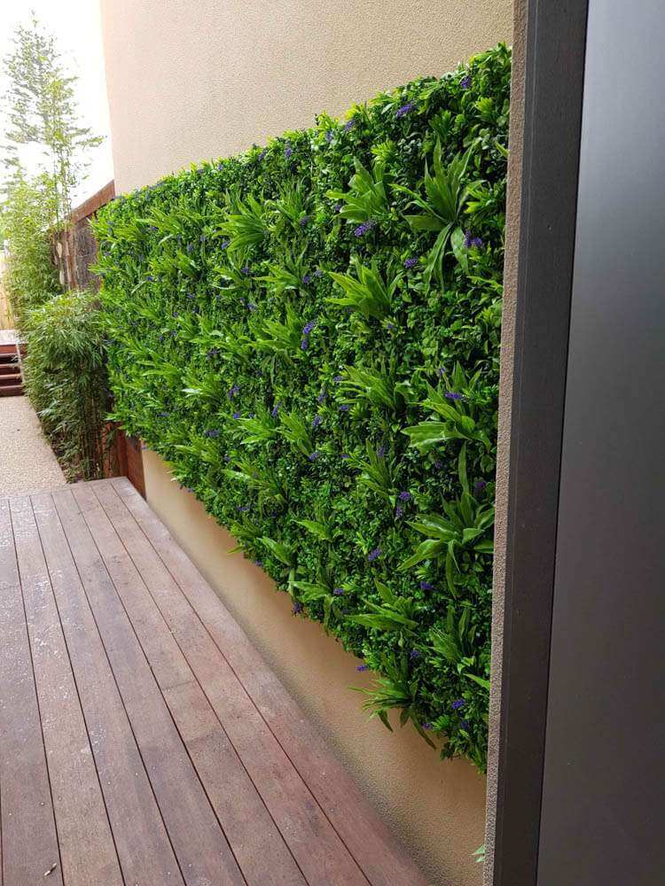 Artificial green wall panel on a building exterior with wooden deck below