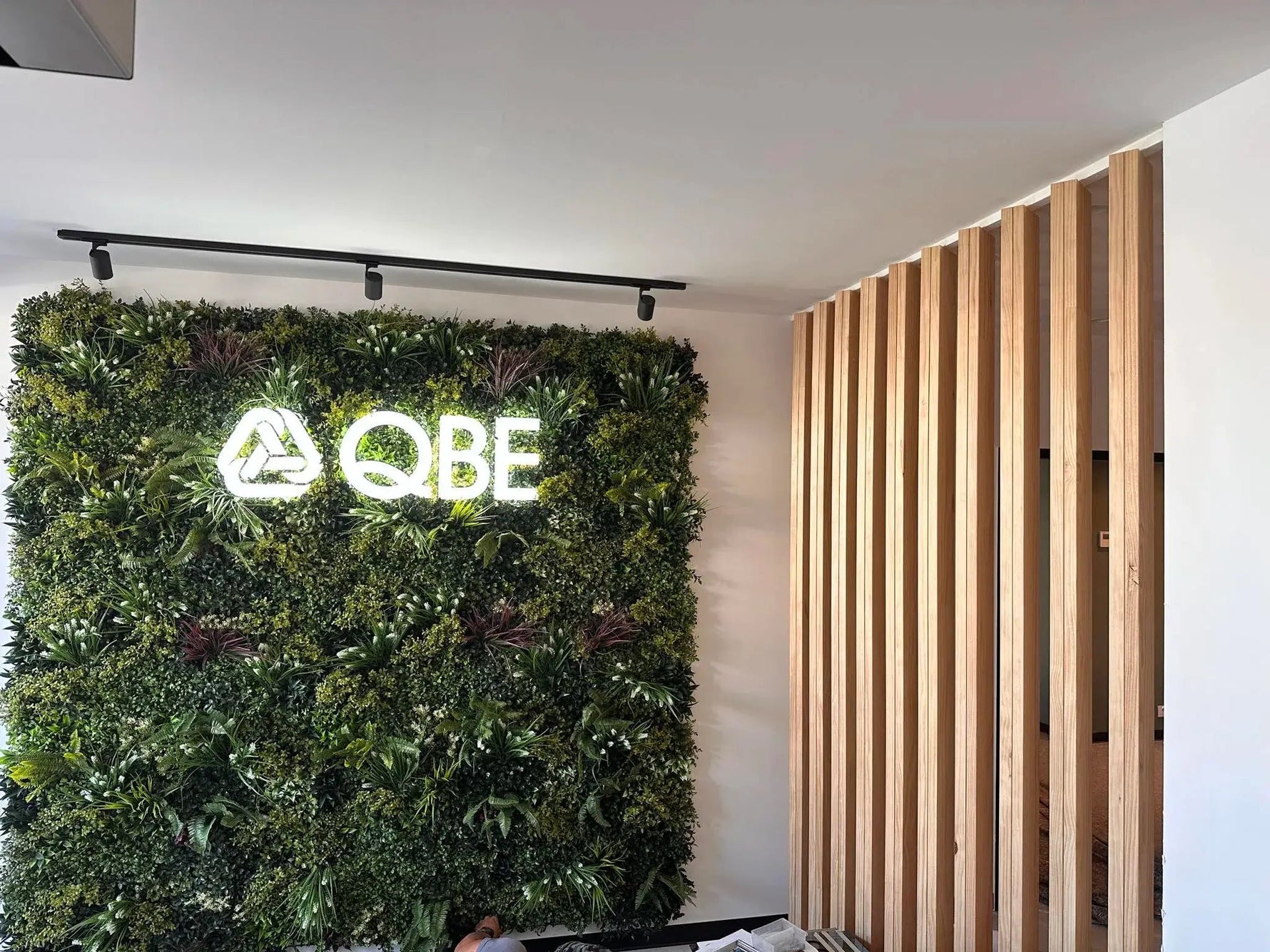 QBE logo on a green wall with wooden slat paneling