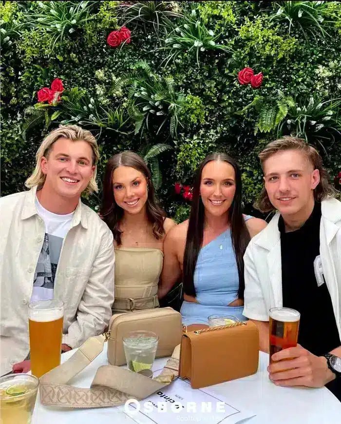 Four friends sitting at a table with drinks and a plant background
