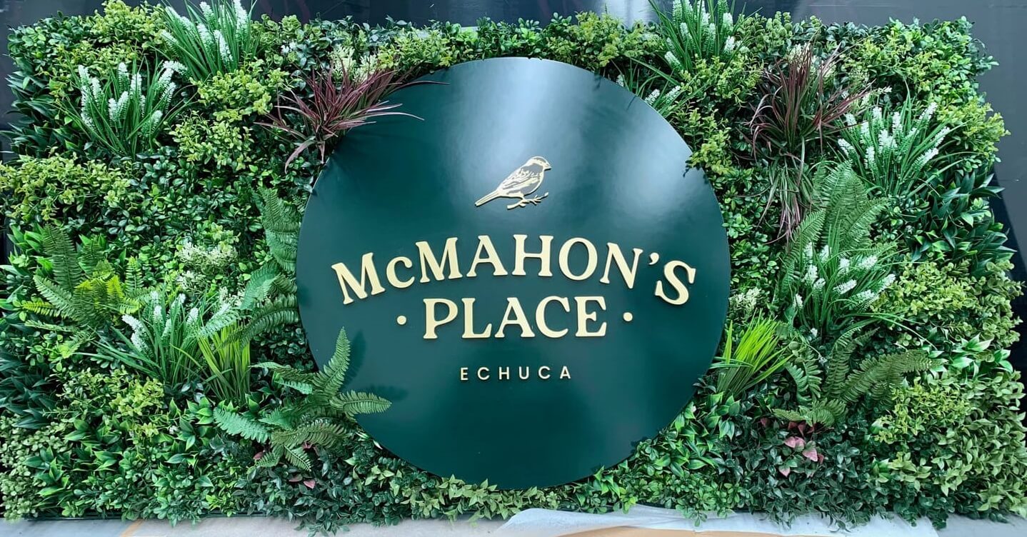 Green sign with 'McMahon's Place Echuca' surrounded by artificial plants