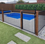 Swimming pool with a black metal and wooden fence in a backyard setting.