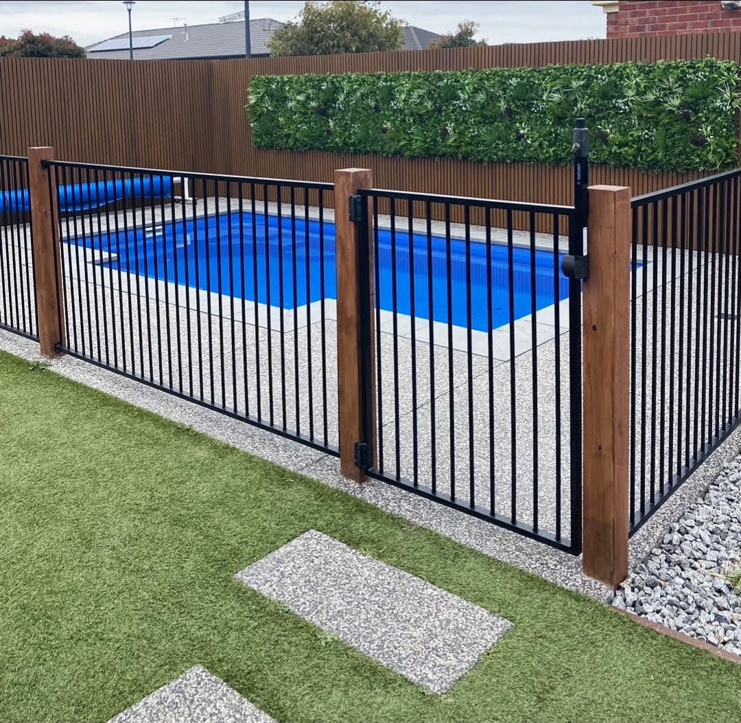 Swimming pool with a black metal and wooden fence in a backyard setting.