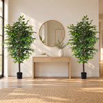 Two tall artificial green potted trees flanking a light wood console table in a bright, modern room with a round gold-framed mirror and a woven rug.