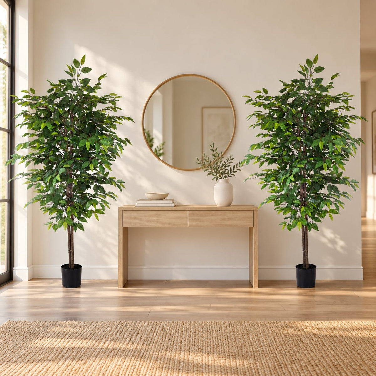 Two tall artificial green potted trees flanking a light wood console table in a bright, modern room with a round gold-framed mirror and a woven rug.