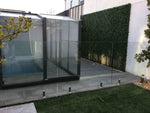 Modern glass pool enclosure with greenery and a building in the background