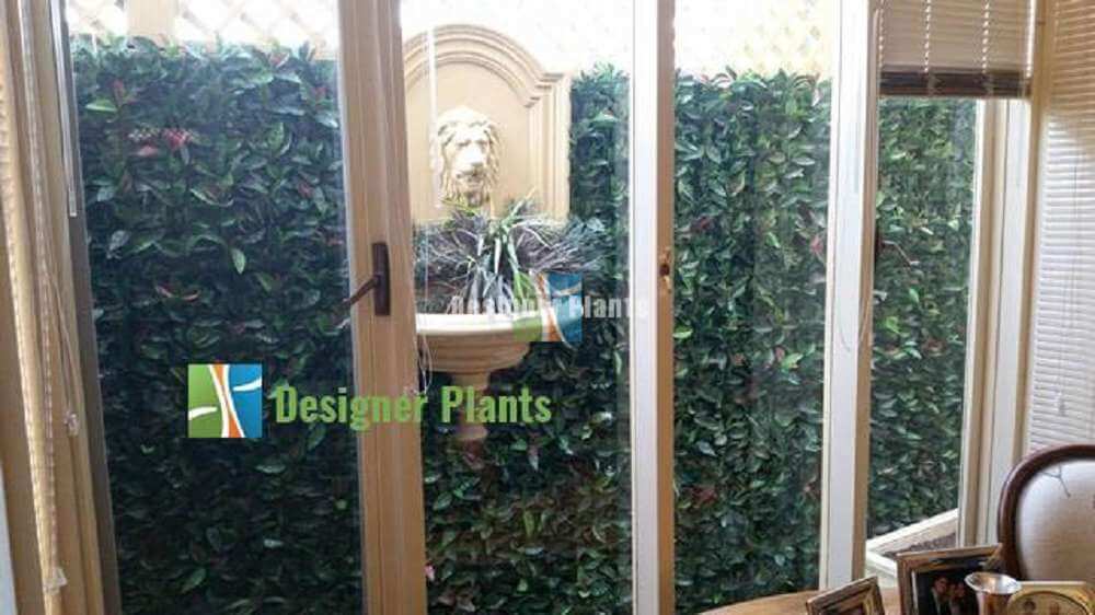 Indoor setting with artificial greenery and a decorative mirror, featuring 'Designer Plants' logo.