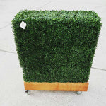 Square artificial hedge plant on wheels with a wooden base against a light background