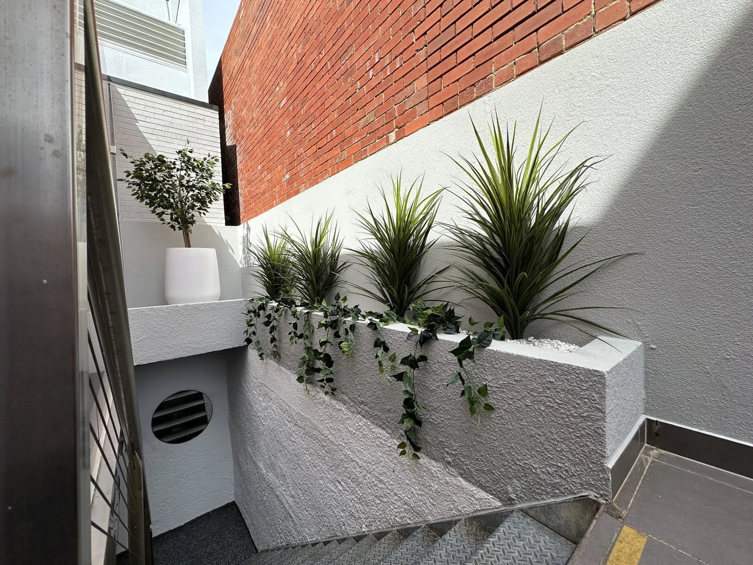 Modern outdoor staircase with plants and a white wall.